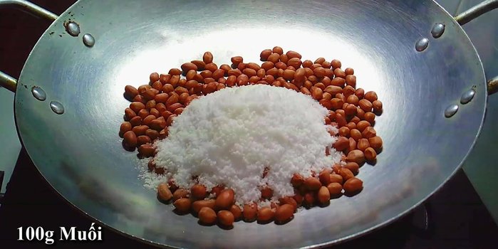 Rang đậu phộng với muối: Cho 150g đậu phộng và 100g muối vào chảo, rang với lửa trung bình thấp đến khi muối khô, vỏ đậu chuyển màu hơi đỏ và hạt đậu vàng giòn.