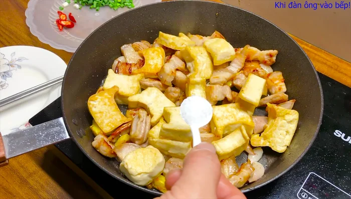 Cho đậu phụ đã chiên vào chảo, thêm mì chính, hạt nêm, nước mắm, ớt (tùy chọn). (490.48)