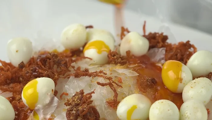 Trộn đều các nguyên liệu: bánh tráng, tép khô, khô bò, trứng cút, muối tôm, nước tắc, dầu màu điều, sa tế, hành phi, lạc rang, rau răm. Trộn nhẹ nhàng để tránh làm vỡ trứng cút.