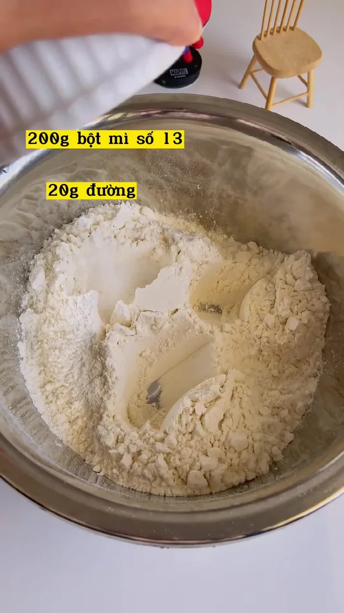 Cho bột mì vào tô, thêm muối, đường, men nở. Lưu ý: cho muối sau men để tránh ức chế hoạt động của men.
