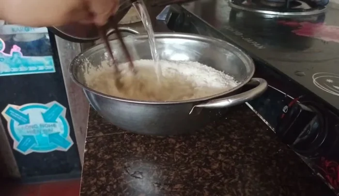 Từ từ đổ nước sôi vào bột sắn, vừa đổ vừa trộn đều tay cho đến khi bột dẻo mịn. (Lưu ý: Dùng nước sôi để tạo độ dẻo và không làm bột bị vón cục).