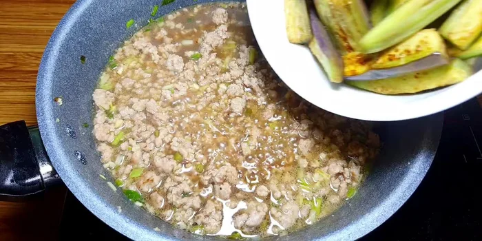 Cho cà tím đã chiên vào chảo, trộn đều với hỗn hợp thịt và gia vị. Nấu thêm 5 phút với lửa nhỏ.
