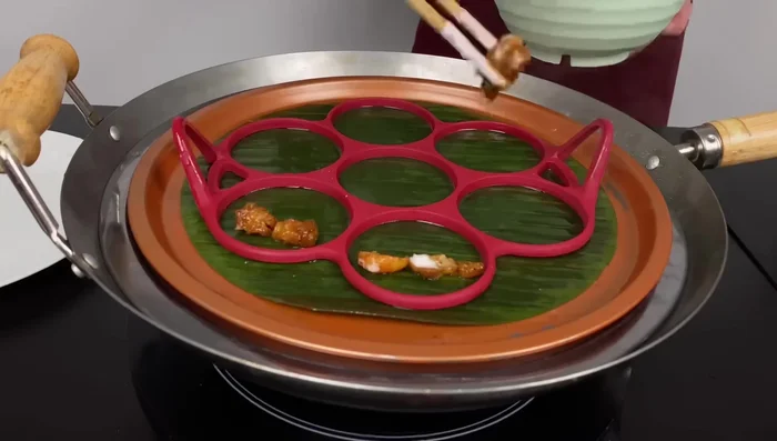 Đặt khuôn bánh lên lá chuối, cho nhân vào khoảng 1/3 khuôn, rót bột vào đến khoảng 2/3 khuôn.