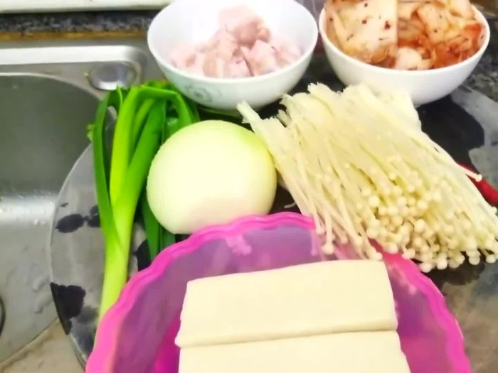 Sơ chế nguyên liệu: Thịt ba chỉ thái miếng 3-4cm. Hành baro phần trắng cắt nhỏ, phần lá xanh cắt khúc 3cm. Hành tây cắt miếng nhỏ hoặc hiếm. Nấm kim châm cắt gốc, rửa sạch, cắt khúc 3-4 đoạn. Đậu phụ cắt miếng vuông nhỏ. Tế cắt bỏ hạt, thái chéo miếng to. Hành củ tím băm nhỏ. Kim chi cắt khúc 3cm.