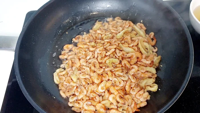 Cho tôm vào chảo mỡ phi hành, rang vàng đều tay, thêm mỡ lợn nếu cần để tôm giòn.