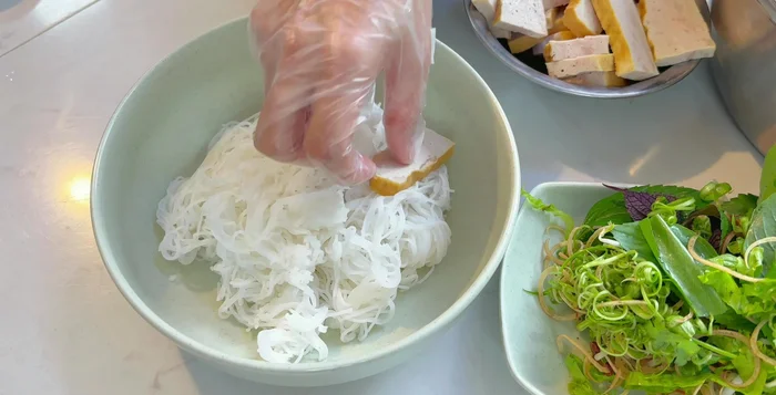Bày rau ra đĩa, cho bún tươi vào tô, xếp chả lụa, hành lá, hành tây lên trên.