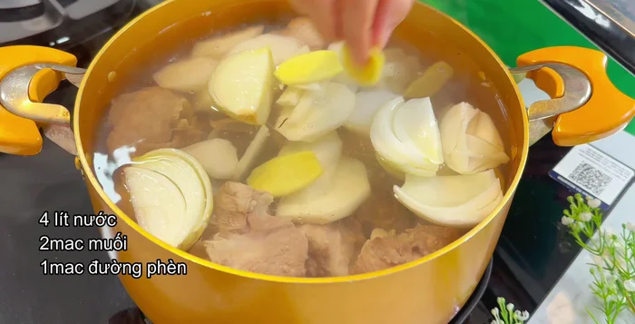 Thêm củ sắn, củ cải trắng cắt lát, hành tây cắt múi, gừng, rễ ngò và gia vị (muối, đường, phèn) vào nồi nước dùng. Hầm xương khoảng 1 tiếng, nhớ vớt bọt để nước dùng trong.