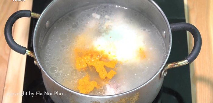 Cho bột nghệ vào nồi nước dùng.