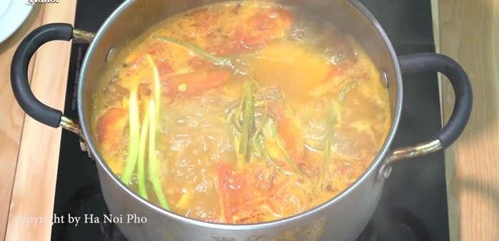 Cho hành lá, rau mùi, cần nước vào nồi nước dùng đang sôi.