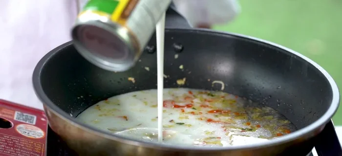 Thêm hỗn hợp sữa tươi, nước cốt dừa, bột nghệ, gia vị (nêm nếm vừa ăn) vào chảo.
