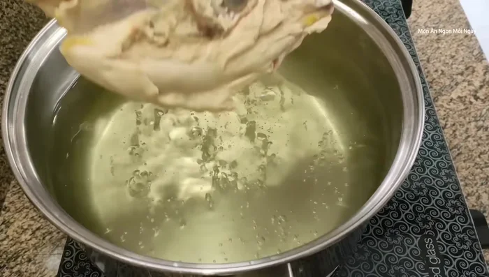 Thêm xương gà, hành tím vào nước dùng đang sôi. Cho thêm chân gà (nếu có) để nước dùng ngọt hơn.