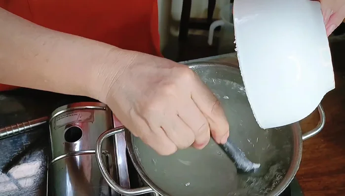 Đổ từ từ hỗn hợp rau câu đang sôi vào khuôn, vừa đổ vừa khuấy nhẹ nhàng để trái cây phân bố đều.