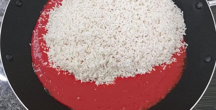Cho nếp vào chảo, trộn đều và xào cho đến khi nước cốt gấc ngấm vào nếp.