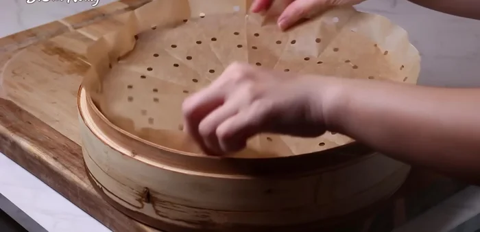 Lót giấy nướng bánh đã cắt lỗ vào xửng tre, cho nếp vào dàn đều, tạo rãnh (505.56).