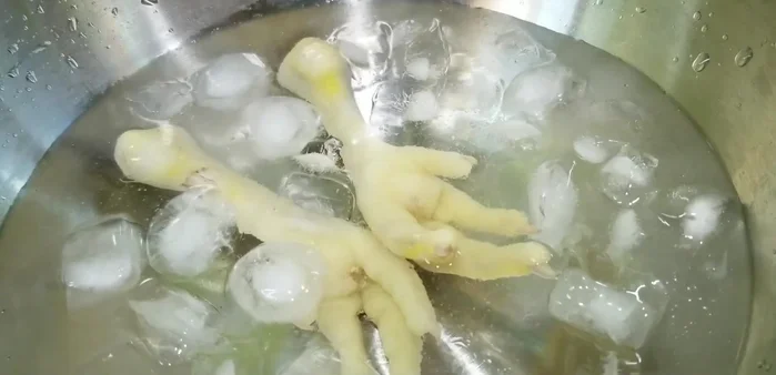 Làm nguội chân gà: Sau khi luộc xong, cho chân gà vào tô nước đá lạnh khoảng 5 phút để da giòn. (288.509)