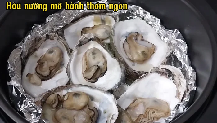 Sau 5 phút, mở nắp nồi chiên, rưới mỡ hành lên hàu, xếp lại hàu cho đều, và nướng thêm 5 phút nữa.