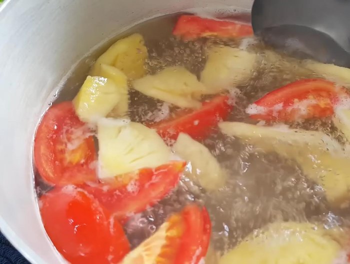 Cho cà chua và trái thơm vào nồi nước dùng đang sôi, nấu khoảng 5 phút.