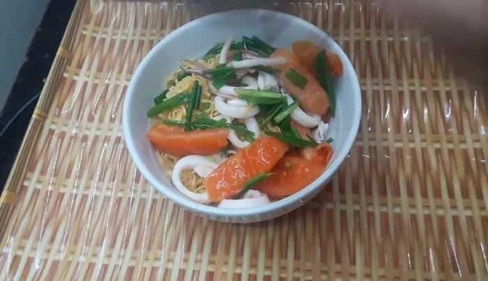 Múc nước sốt cà chua, mực lên trên mì tôm.