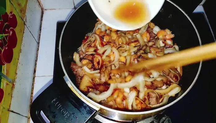 Đổ hỗn hợp nước cốt: Đổ hỗn hợp nước mắm đã pha vào, đảo đều. Nhỏ lửa để nước sốt thấm đều. (281.18)